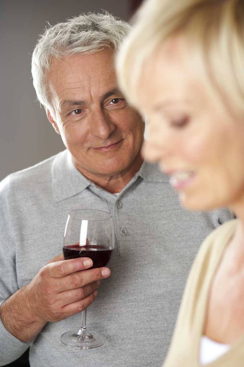 满头白发的男子拿着装满红酒的杯子微笑的看着妻子