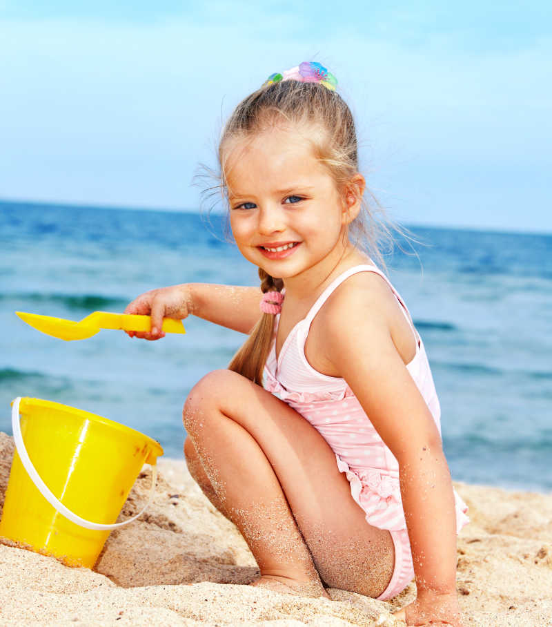 海滩上用黄色的铲子和桶玩沙子的小女孩