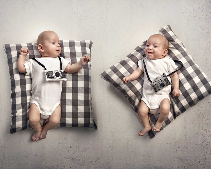 双胞胎婴儿躺在方枕上带着相机饰品
