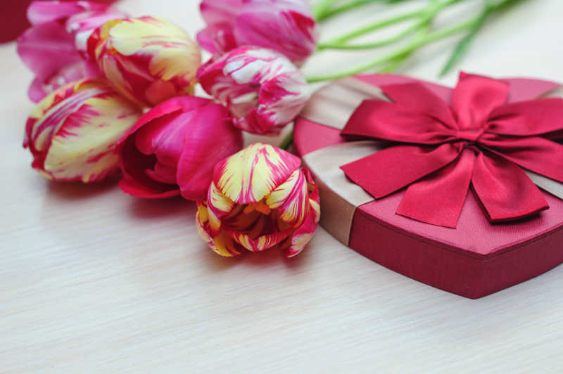 木桌上的郁金香花束和桃心形状的蝴蝶结礼盒