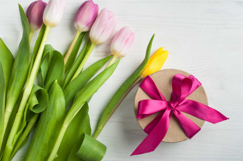 木桌上的郁金香花束和绑着粉色丝带的圆形礼盒
