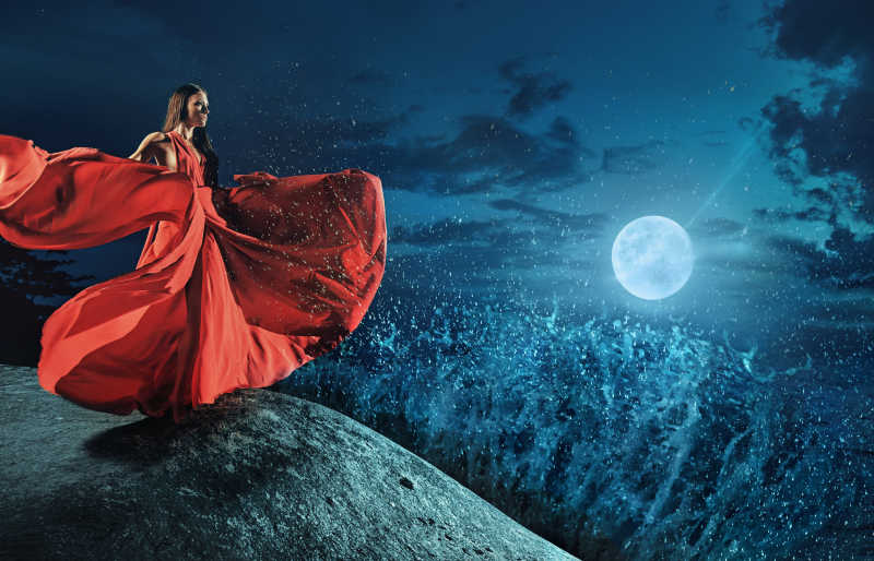 站在悬崖边上穿着红色礼服翩翩起舞的美丽女人