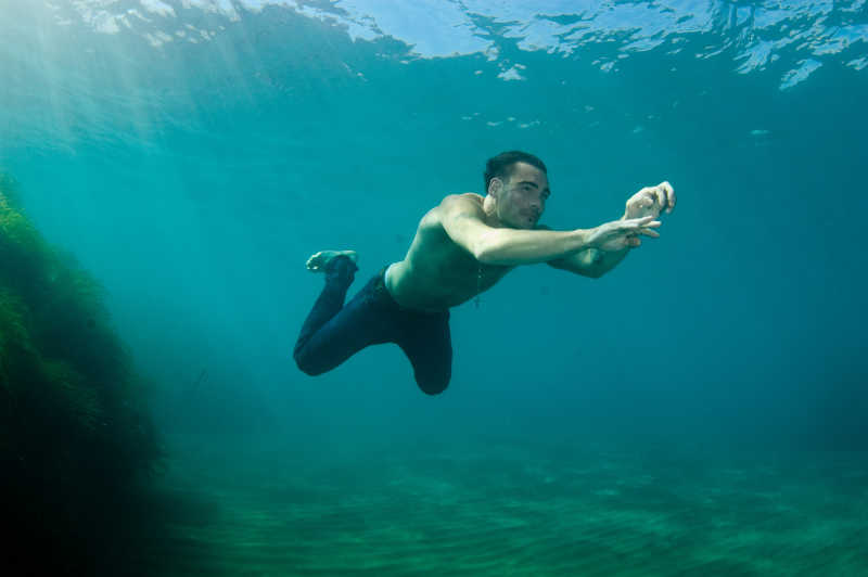 穿着裤子在水里游泳的男人