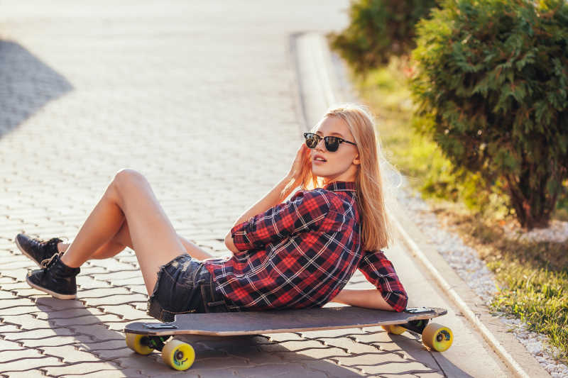 阳光下坐在地上靠着滑板的时尚女孩