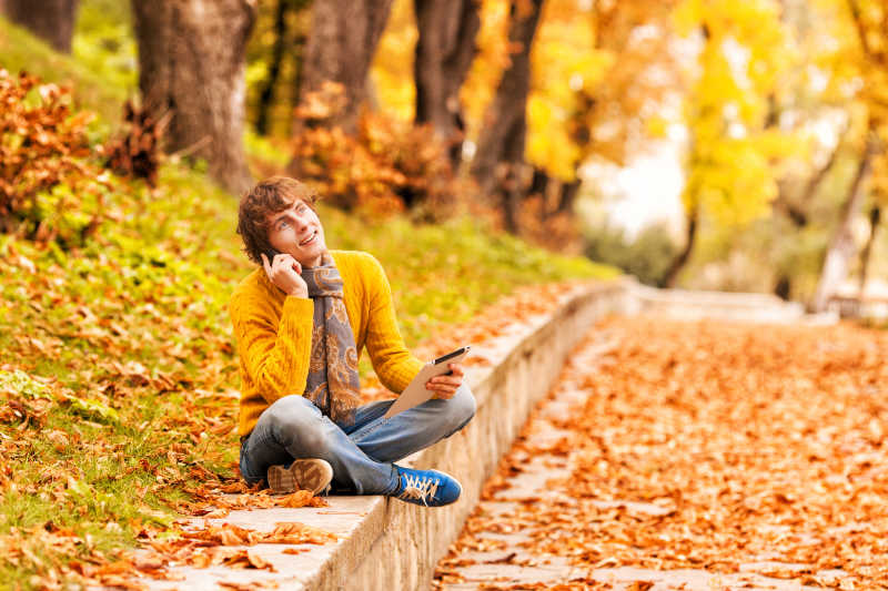 秋天公园里坐在路边打电话的年轻男人