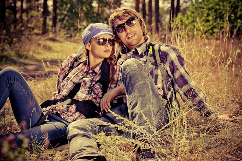 穿着格子衬衫和牛仔裤的年轻夫妇坐在草地上