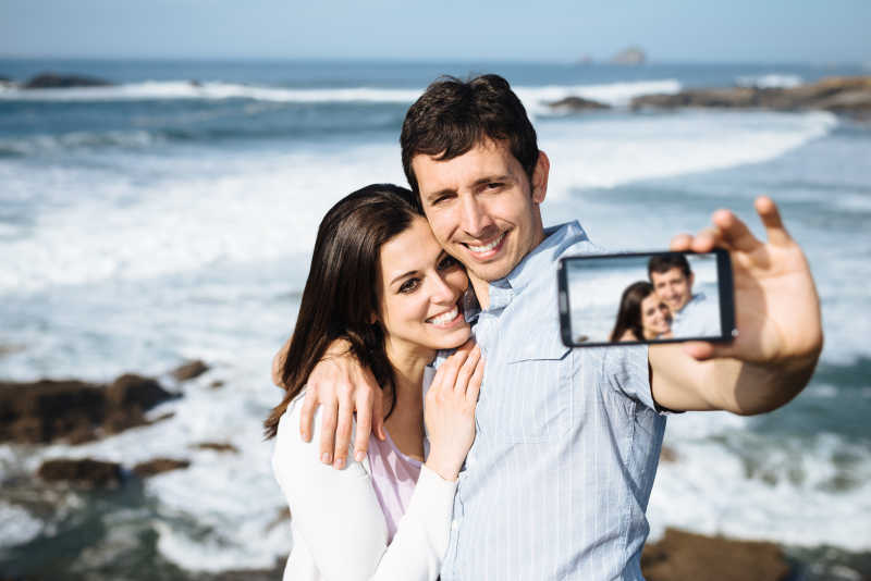 年轻的夫妇在海边用手机自拍