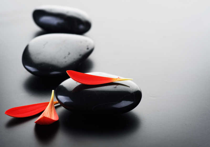 灰色背景下的黑色鹅卵石和红色花瓣