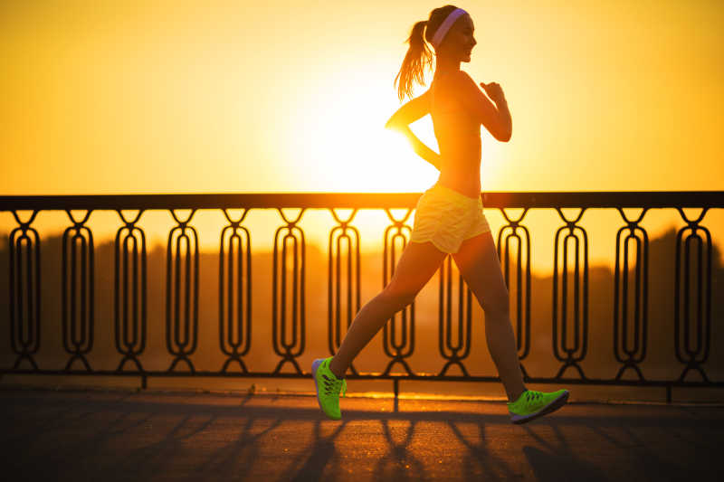 跑步者在日出时在阳光明媚的阳光下慢跑
