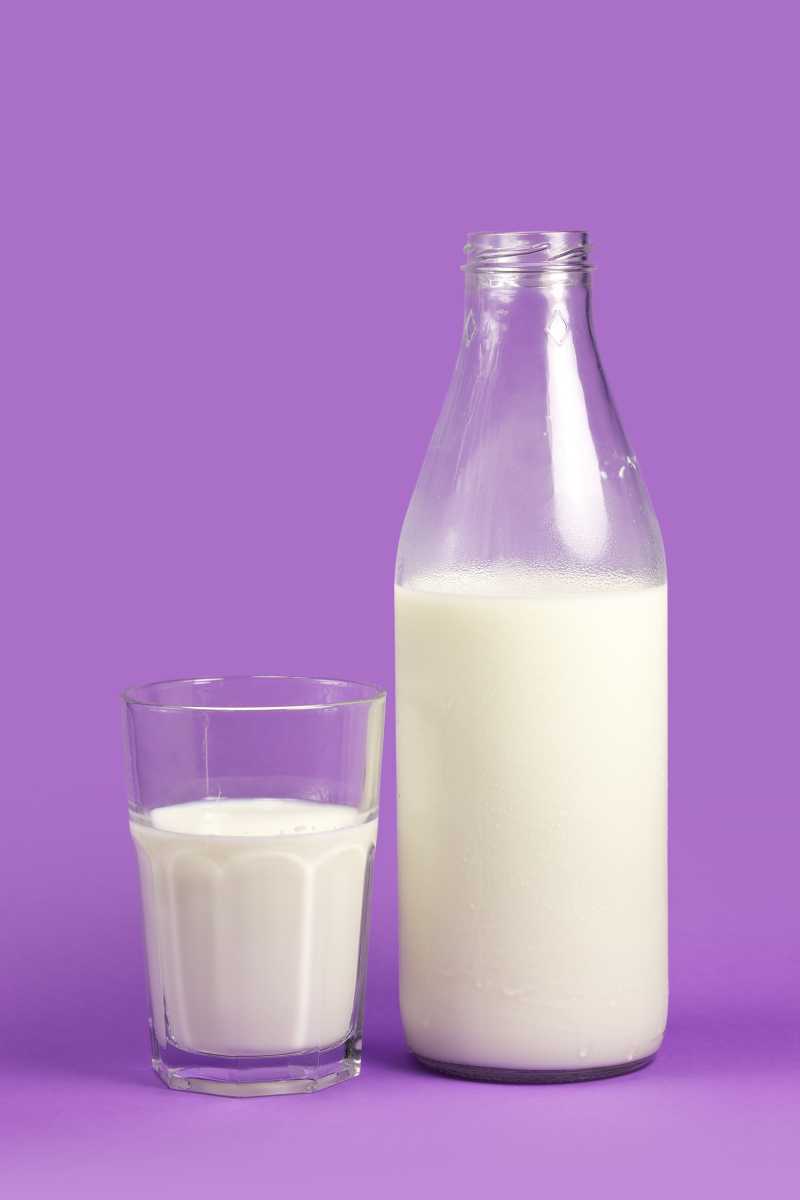 紫色背景下的牛奶瓶和牛奶杯