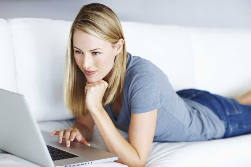 年轻女子躺在沙发上使用笔记本电脑