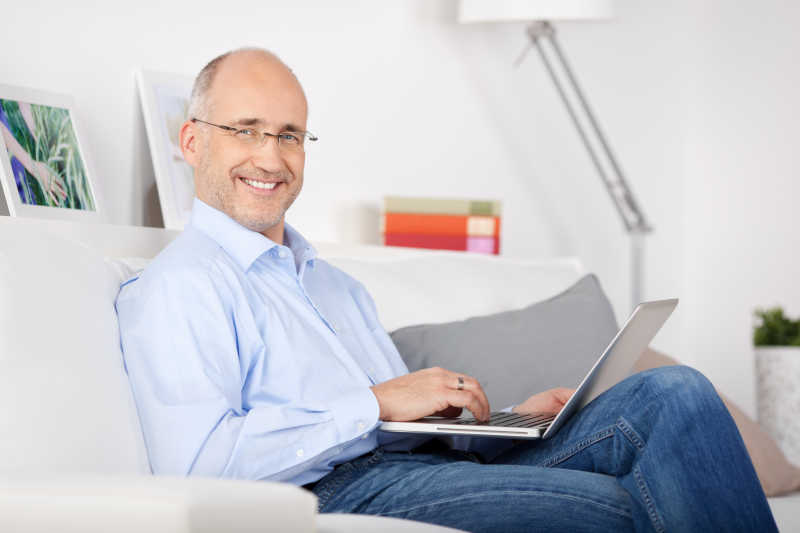 微笑的男人坐在沙发上玩笔记本电脑