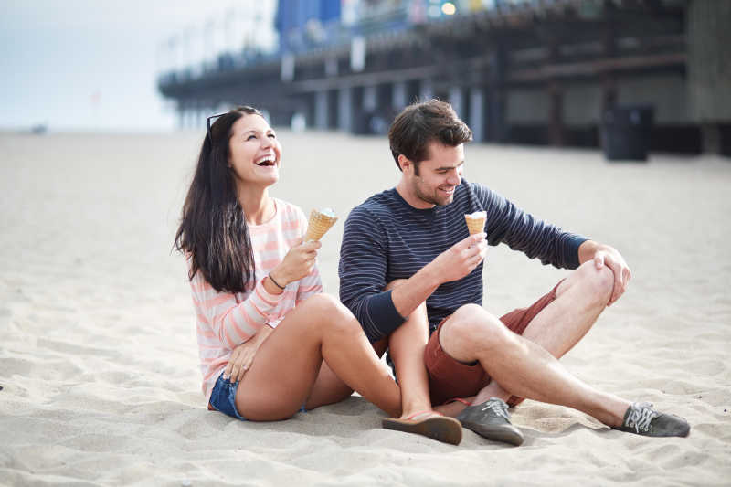 坐在沙滩上吃甜筒的情侣