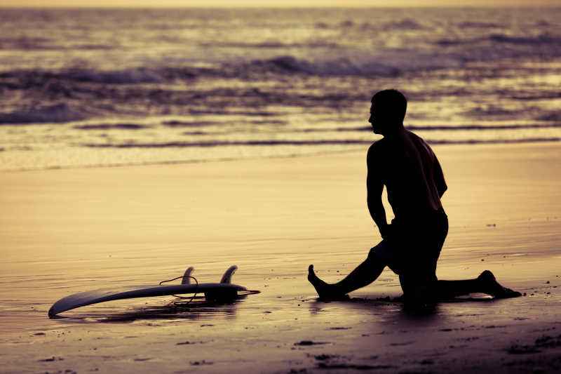 夕阳下的冲浪者将滑板放在沙滩上