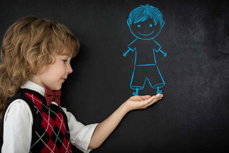黑板前的孩子拿手比划着黑板上画着的小男孩