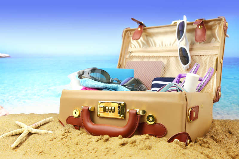 沙滩上放着各种物品的行李箱
