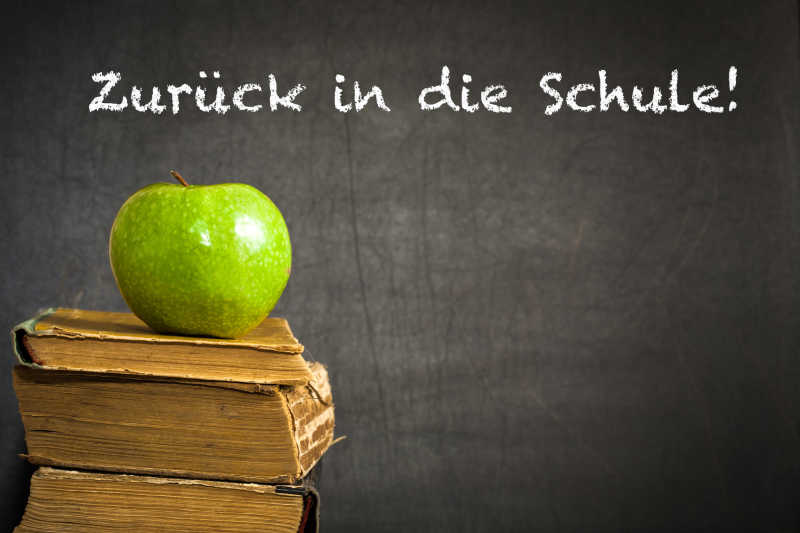 写着重返校园德语字母的黑板前旧书本上的青苹果