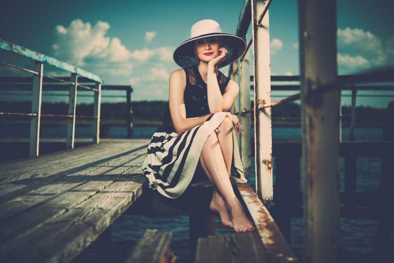 美丽的女人戴着帽子坐在码头上