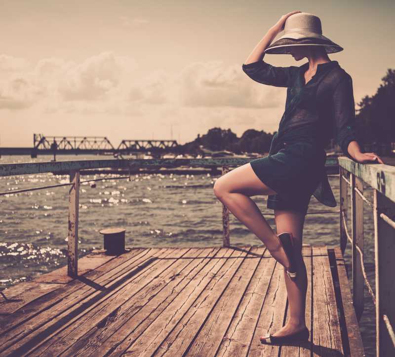 戴着白帽子站在旧木码头上的时髦女人