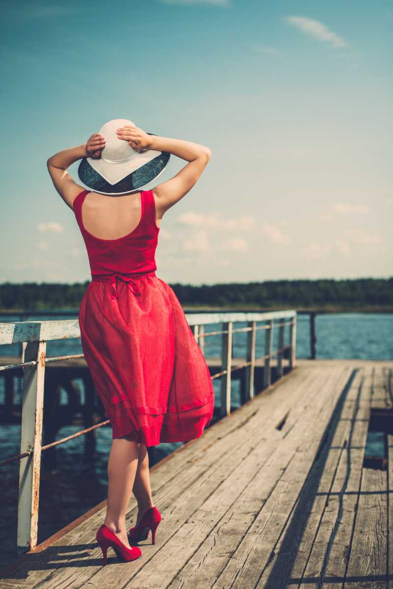 码头边的时尚美女穿着红色裙子和白色帽子