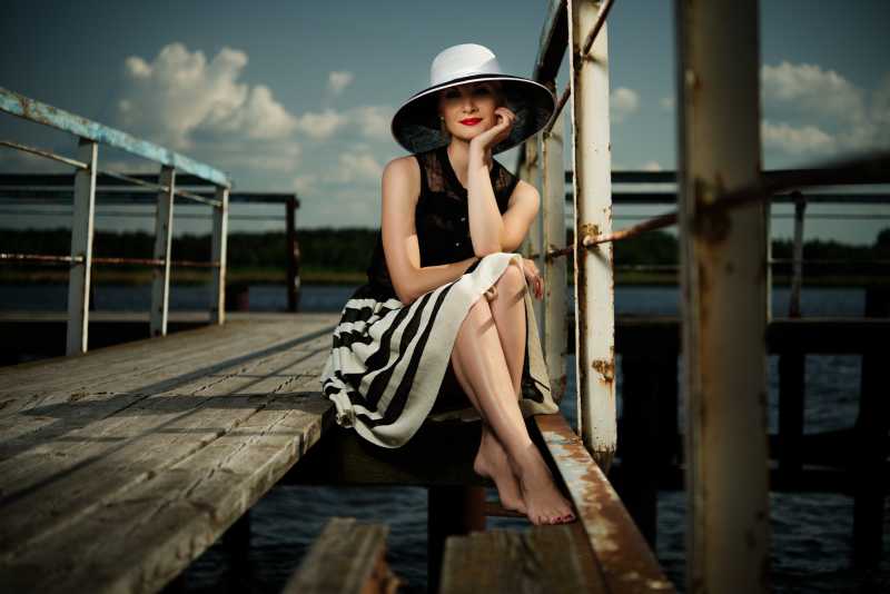 美丽的女人戴着帽子坐在码头