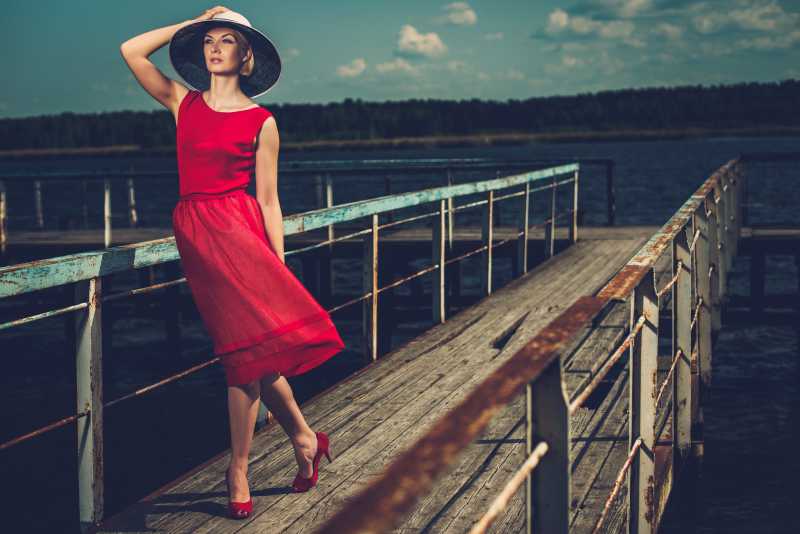 戴着白色帽子和红色衣服的时髦女人在老木头码头上