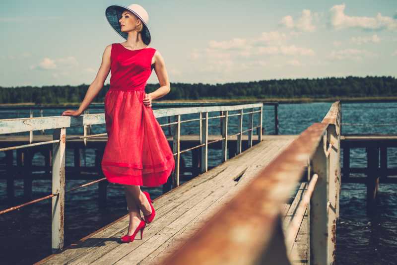 戴着白色帽子穿红色裙子的时髦女人在码头