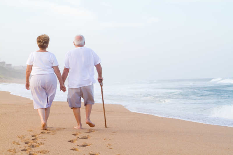 老夫妇手牵手在海滩散步