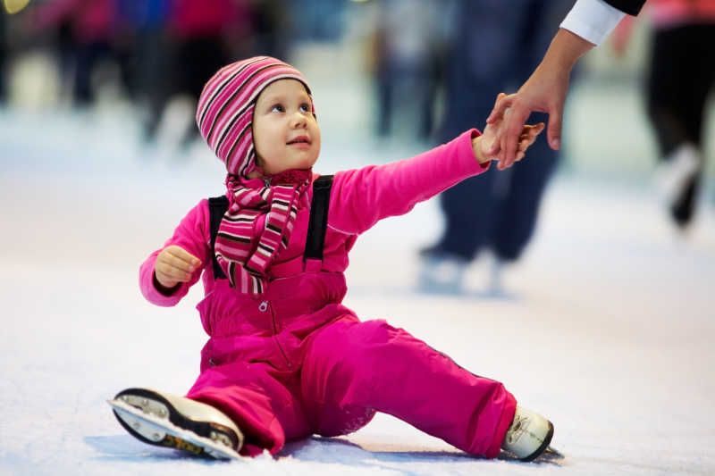 妈妈的手帮助溜冰场上可爱的小女孩