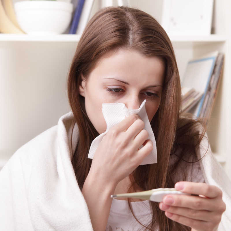披着毯子用手捂拿纸巾住鼻子的女病人观察体温计度数