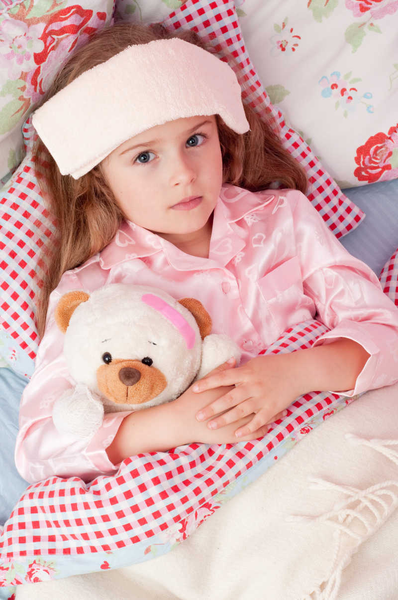 生病的女孩躺在床上抱着泰迪熊
