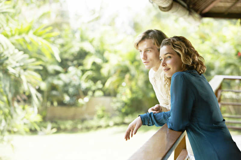 年轻的夫妇靠在阳台的栏杆上欣赏风景