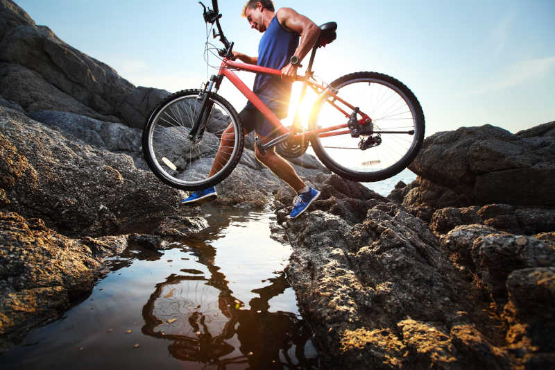 年轻运动员扛着自行车过山间石头地带