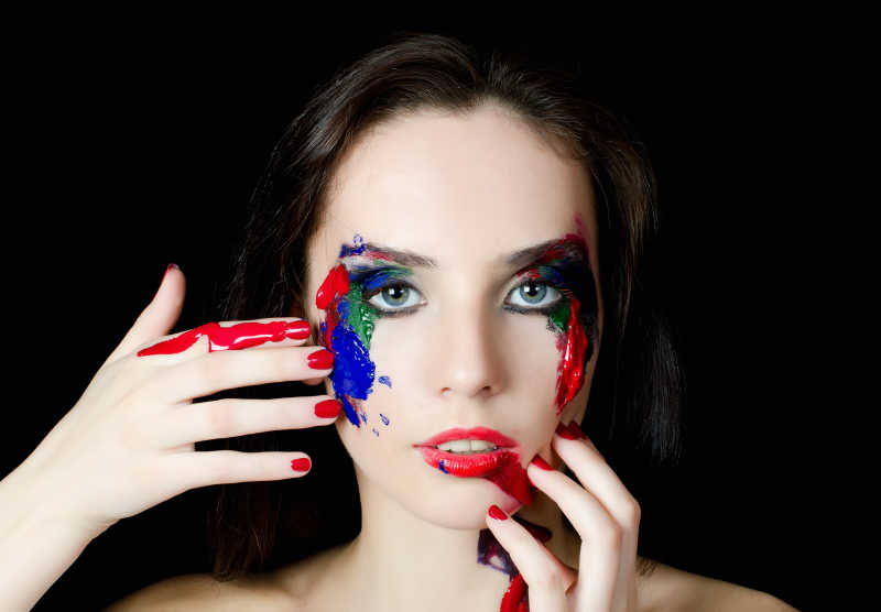 黑色背景下用手在脸上涂颜料的女人