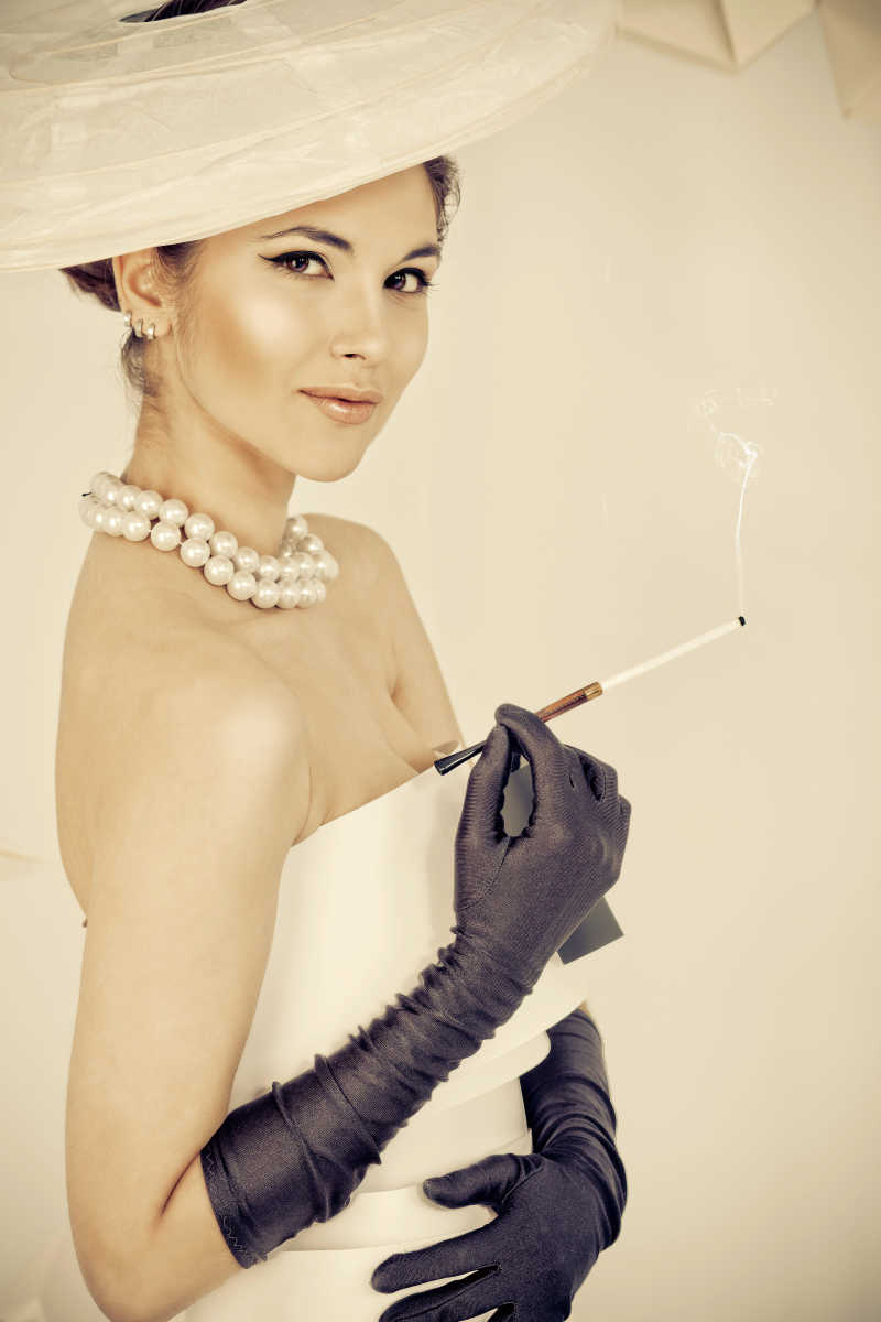 一个穿着纸衣服的带黑色手套的漂亮女人手拿点燃的香烟