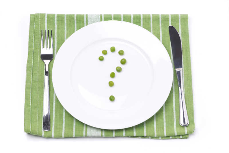 绿色餐巾上白色盘里的绿色豌豆问号