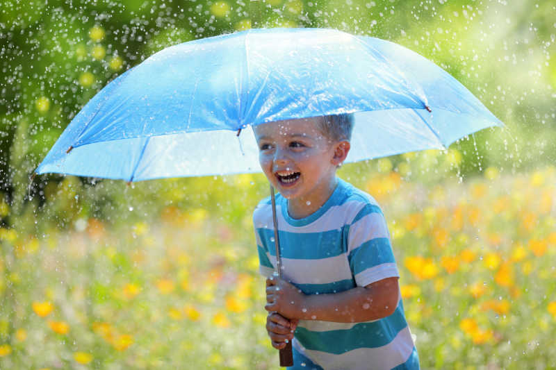 雨中撑着蓝色雨伞的小男孩