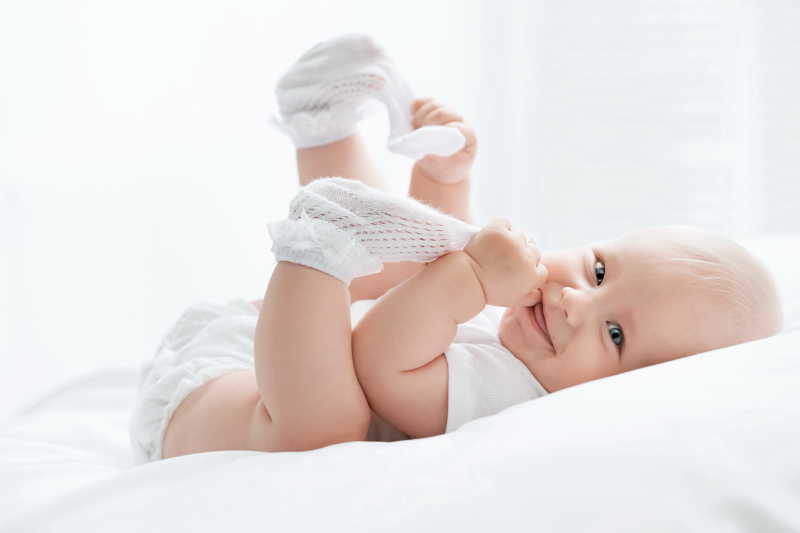 白色背景下白色床上拽着白色袜子微笑的婴儿