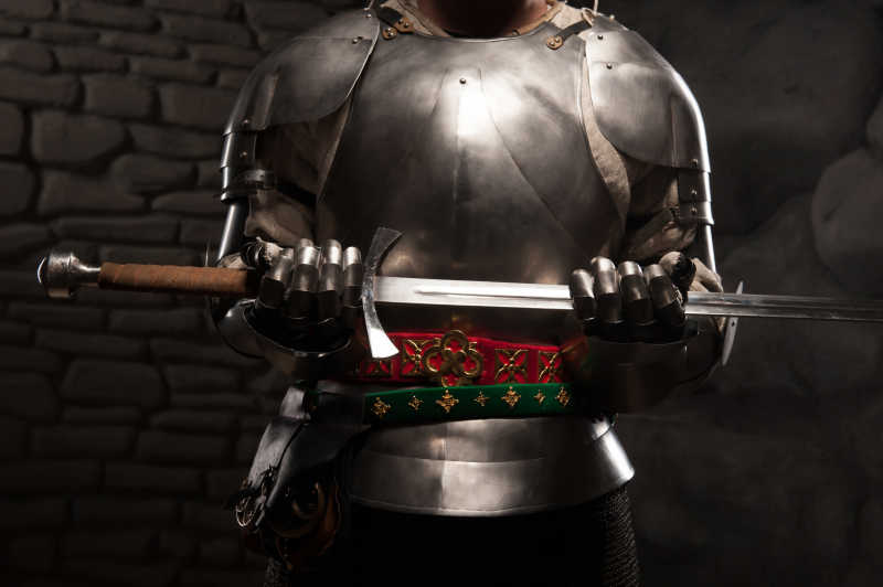 在黑暗的石头墙背景中骑士穿着盔甲手持利剑