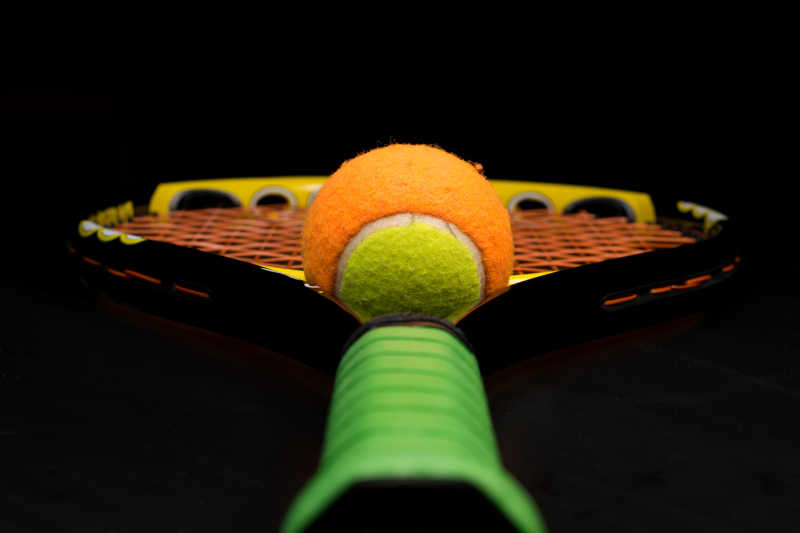 黑色背景下的绿色握柄的网球拍和网球