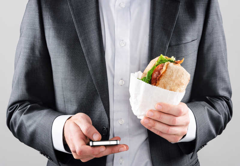 一手拿着三明治一手拿着手机的男人