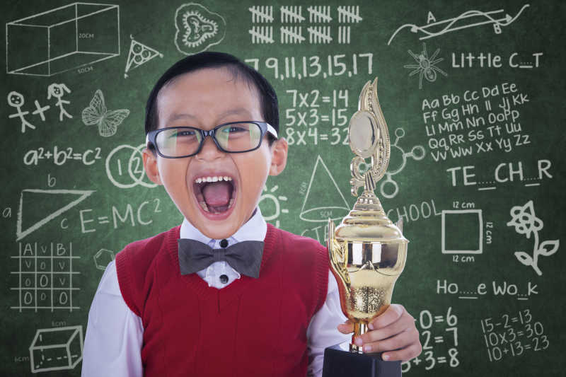 兴奋的男孩在教室黑板前拿着奖杯尖叫