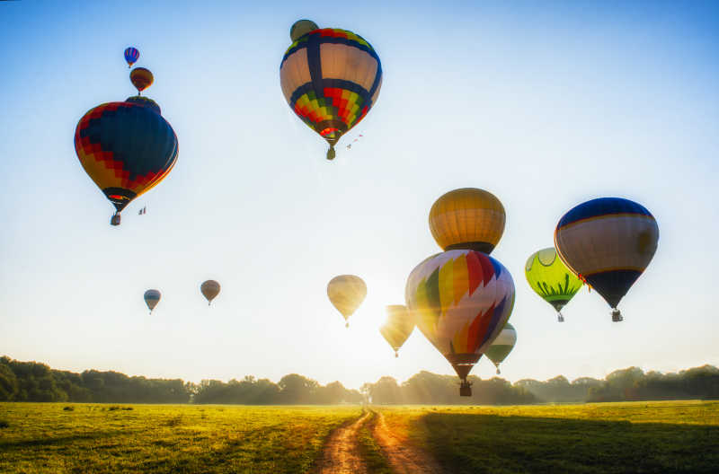 晴天阳光下飞跃农田的五彩缤纷的热气球