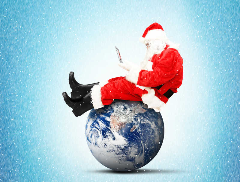 圣诞老人拿着笔记本电脑坐在地球上