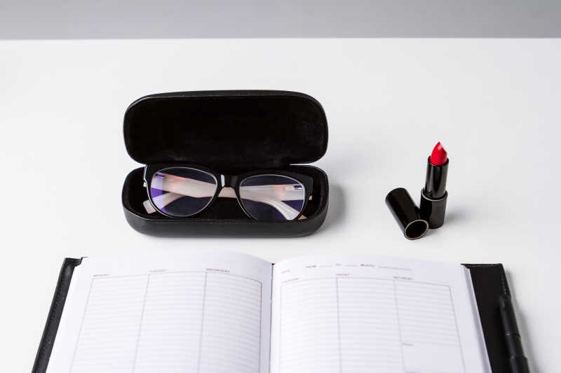 白色背景下的笔记本和口红旁边的眼镜