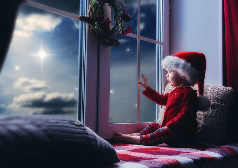 坐在窗边的带着圣诞帽子的小女孩看夜晚的天空