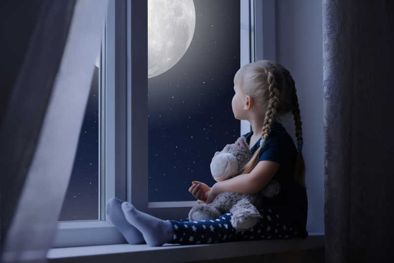 抱着玩具熊的小女孩安静的坐在窗户边上