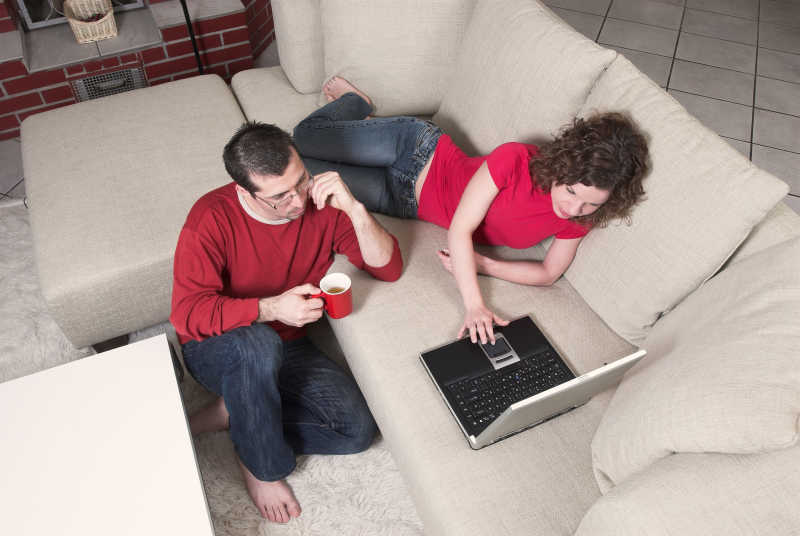 年轻的夫妇在沙发上放松一起看笔记本电脑