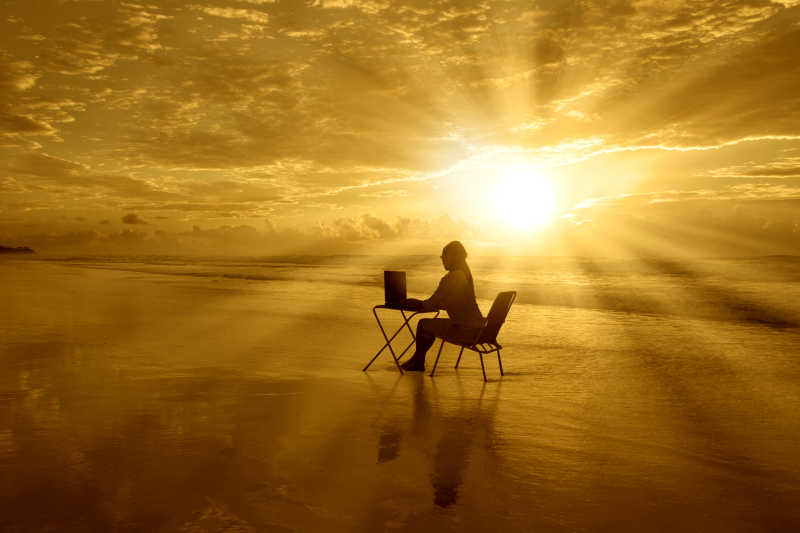 落日下的海滩一个女孩在那里操作着笔记本电脑