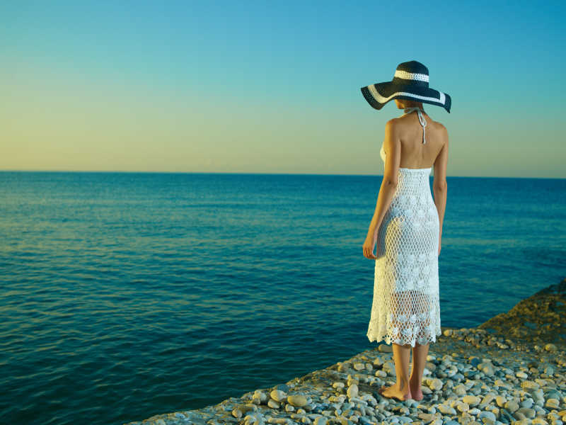 站在沙滩上戴着帽子的优雅的年轻女子